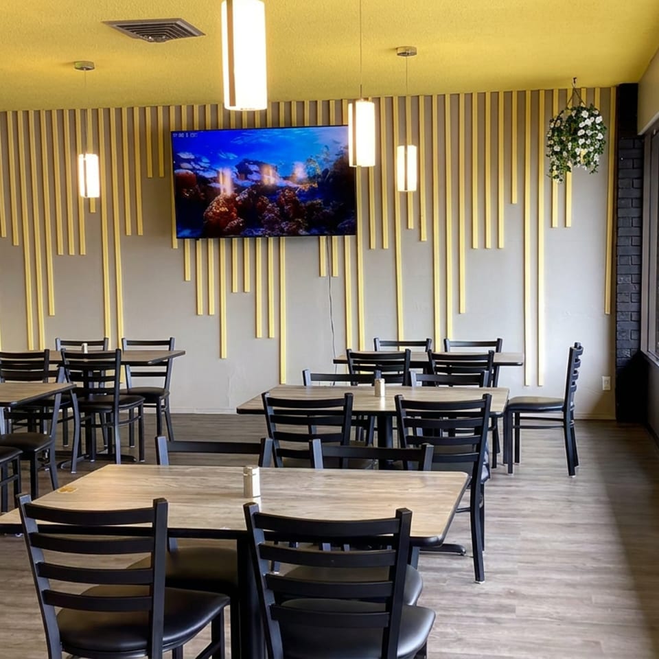 Bright modern restaurant dining area with black tables and chairs, yellow accents, pendant lights, artwork, and large windows.