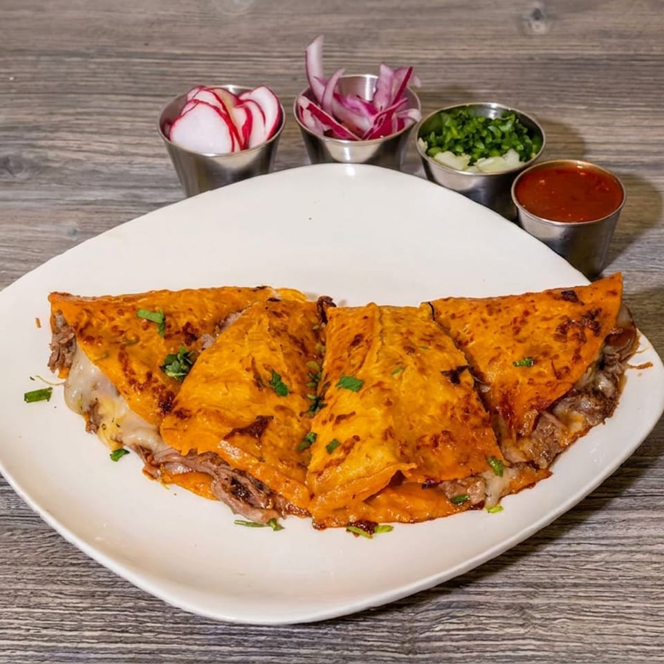 Plate of folded, cheesy orange quesadillas with shredded meat, garnished with herbs and served with radishes, onions, greens, and red salsa.
