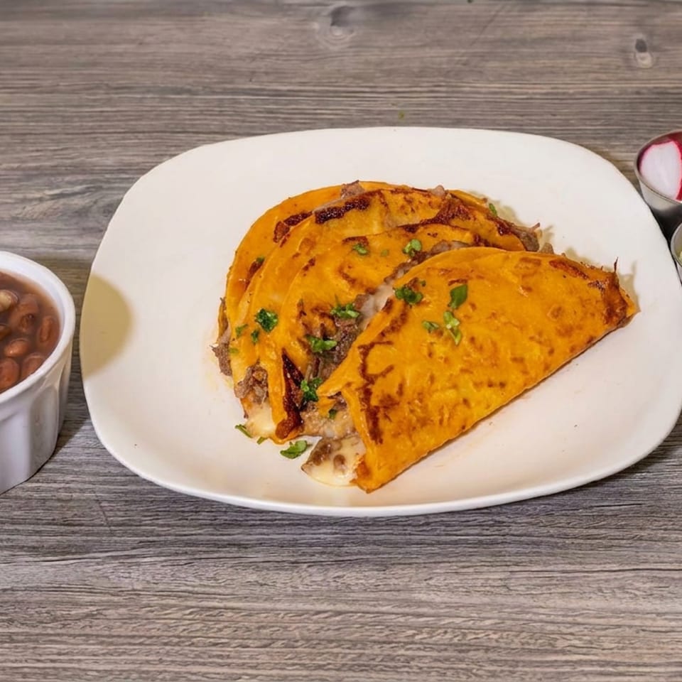 Cheesy folded tacos garnished with cilantro, served with pinto beans, pickled onions, radishes, and red salsa on a wooden table.